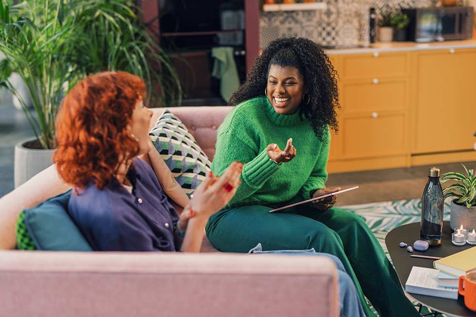 Two women sitting on the couch speaking and smiling